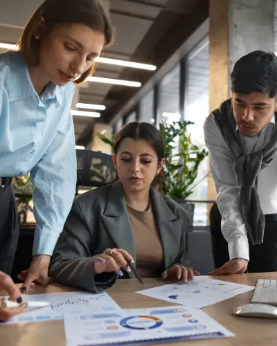 three business professionals collaborating at a desk, engaged in discussion and reviewing documents together