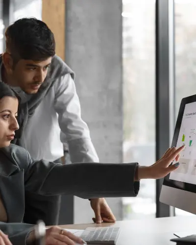 two individuals collaborating on a computer in a modern office setting, focused on their work